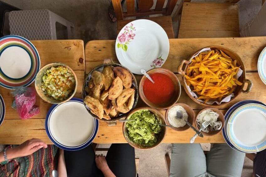Een houten tafel met diverse gerechten, waaronder chips, salsa, guacamole en een schaal met mais. 5