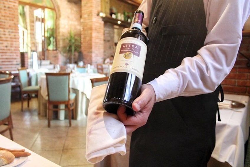 Una persona sosteniendo una botella de vino en un restaurante. 1