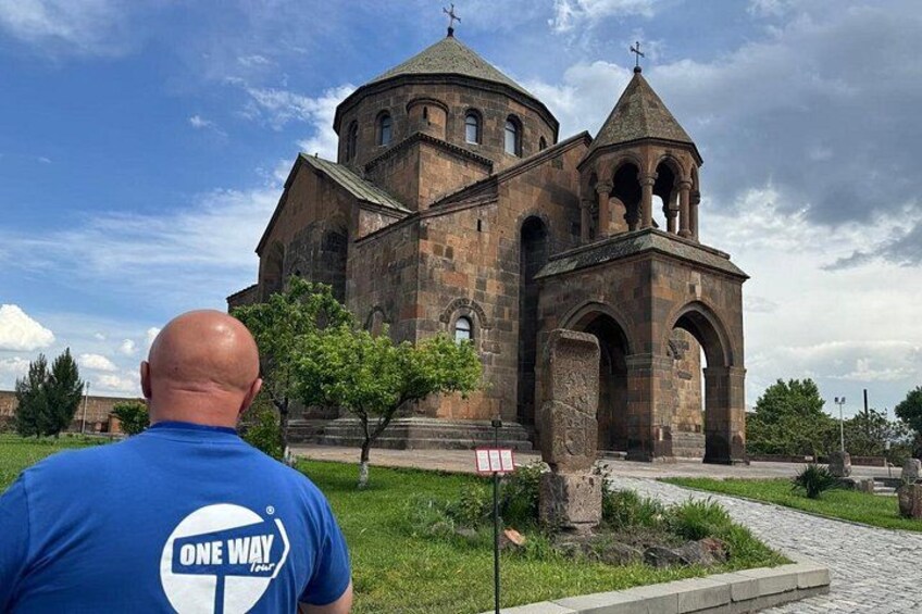 A man in a blue shirt with a logo, standing in front of a historic church with a bell tower. 3