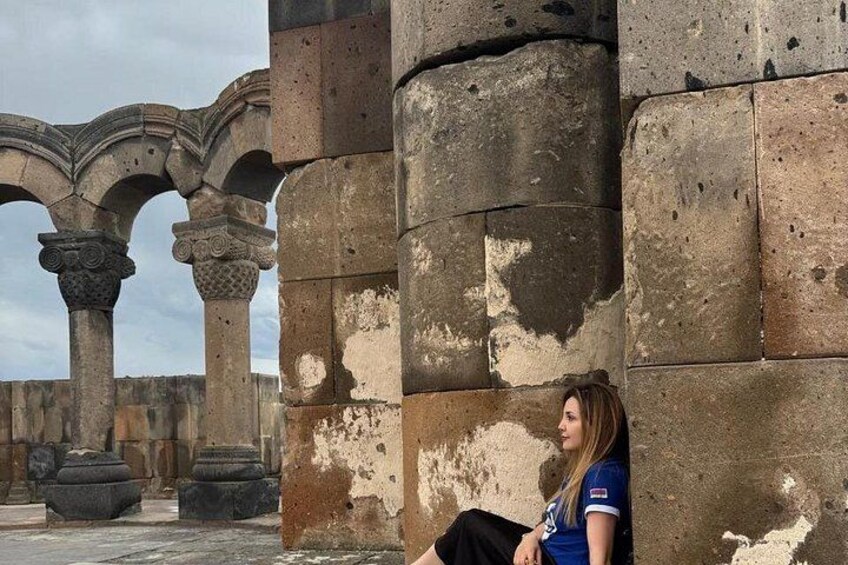 A person sitting on a stone wall with ancient columns in the background. 2
