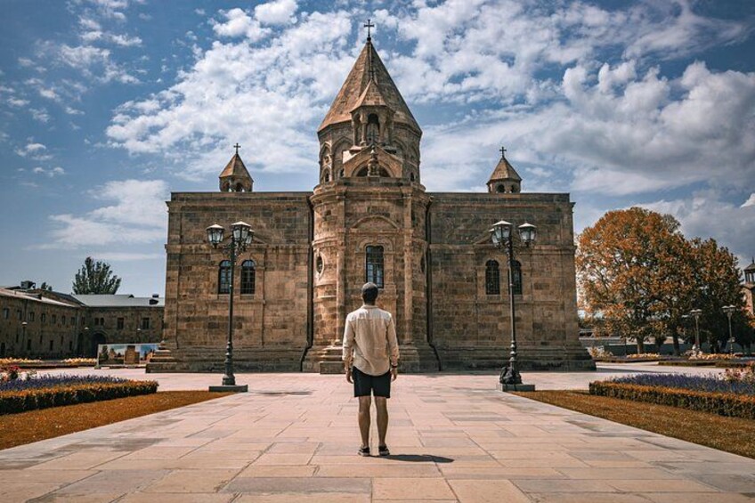 A person standing in front of a historic building with a prominent tower and arched windows. 4