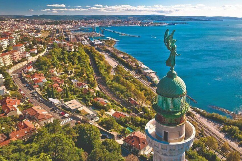Un paysage urbain côtier avec une tour imposante surmontée d’un dôme vert et ornée d’une statue, le tout entouré d’une végétation luxuriante et d’une mer d’un bleu limpide. 2