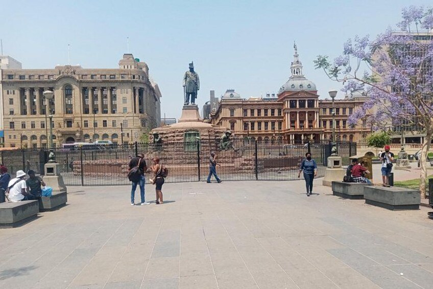 A plaza with a statue, a large building, and people walking. 5