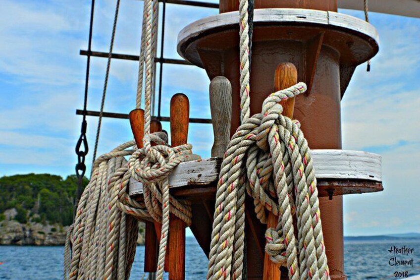 A ship's wheel, ropes, and a rocky shoreline in the background. 2