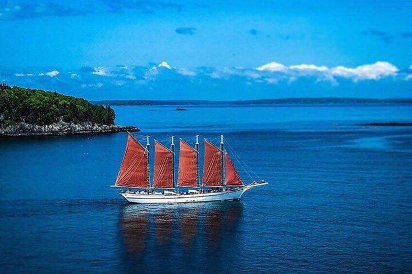 A sailboat with red sails on calm water, surrounded by a clear blue sky and a distant shoreline. 1