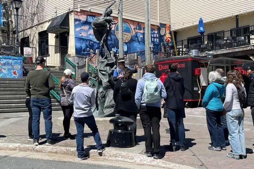 A group of people standing on a sidewalk near a statue and a taco truck. 2