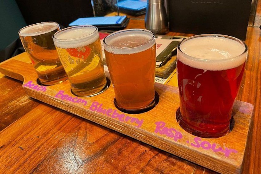 Four glasses of beer on a wooden tray with text. 5