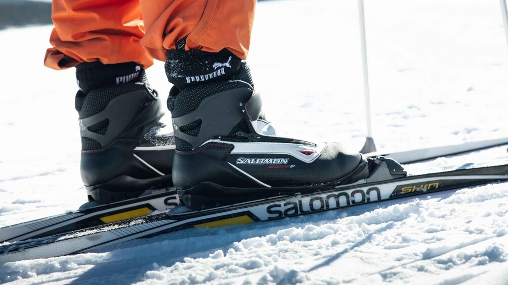 A pair of black and white Salomon skis with orange pants and black socks. 2