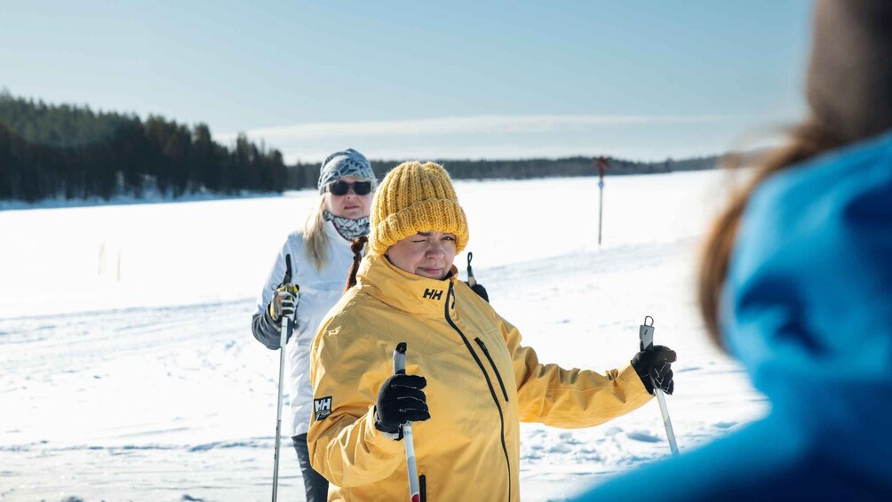 A person in a yellow jacket skiing on snow with a clear sky and trees in the background. 1