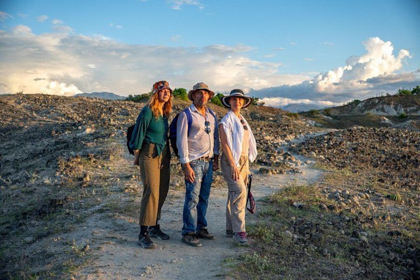 Three people standing on a dirt path in a rocky landscape with hills in the background. 3