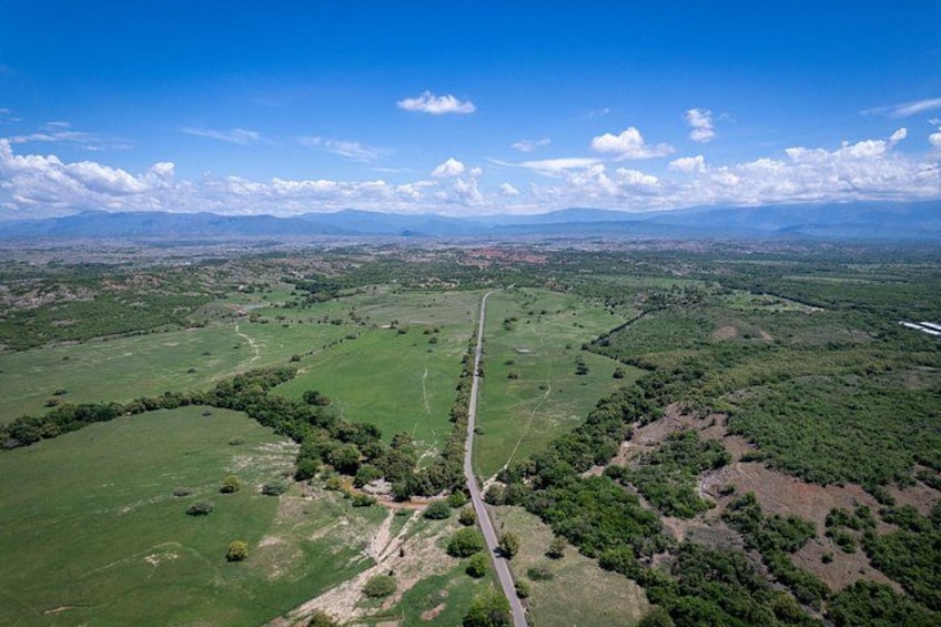 A rural landscape with a winding road, green fields, and distant mountains under a clear sky. 1