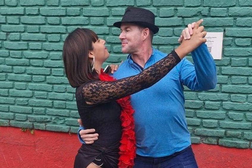 Two people dancing in front of a green brick wall. 2