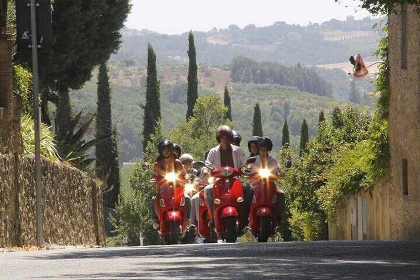Un groupe de personnes sur des scooters rouges, sur une route bordée d’arbres et entourée de collines. 1