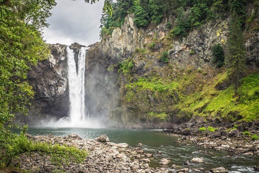 A waterfall cascading into a river surrounded by rocky cliffs and lush greenery. 1