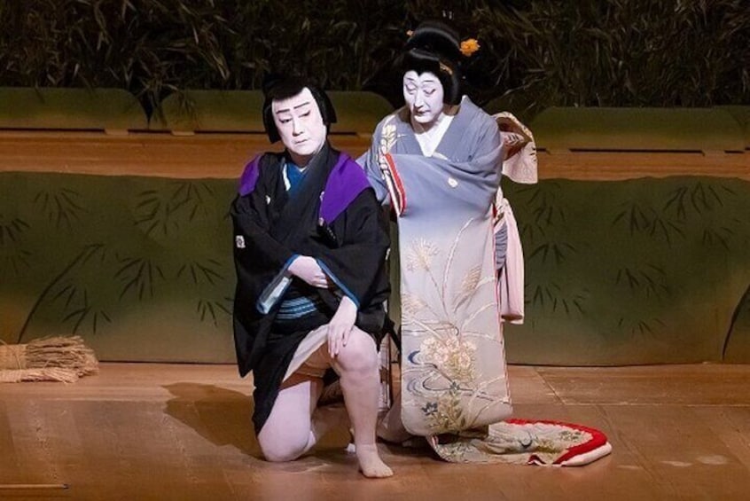 Two individuals in traditional Japanese attire on a stage with a backdrop of bamboo. 1