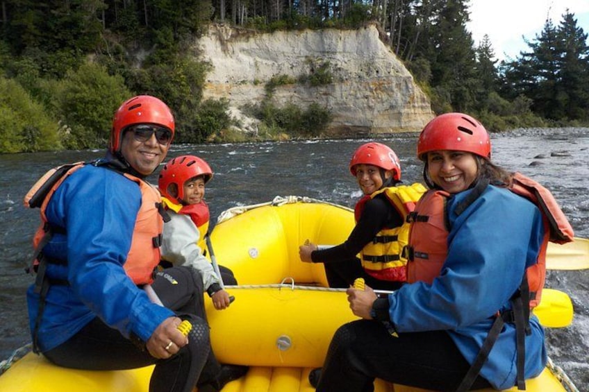 Un grupo de personas en un bote amarillo flotando en un río, con un risco rocoso al fondo. 1