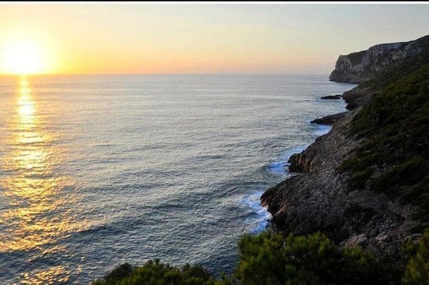 A coastal landscape with a cliff, ocean, and a setting sun. 5