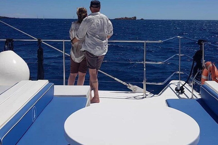 A couple standing on a boat deck, a railing, and the ocean. 2