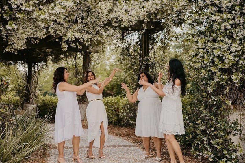 A group of women in white dresses standing under a floral archway in a garden. 4
