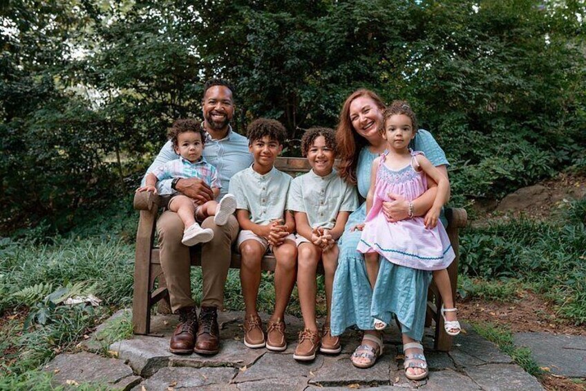 A family of six on a wooden bench in a wooded area. 3