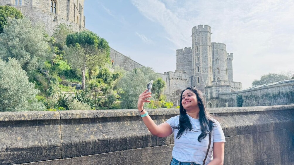 A person taking a selfie with a historic stone bridge and castle in the background. 3