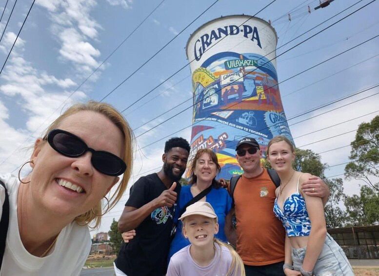 A group of people posing in front of a large water tower with colorful murals. 2