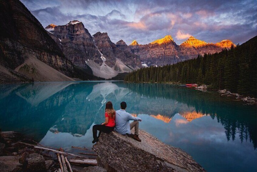 A couple sitting by a calm lake with mountains in the background. 5