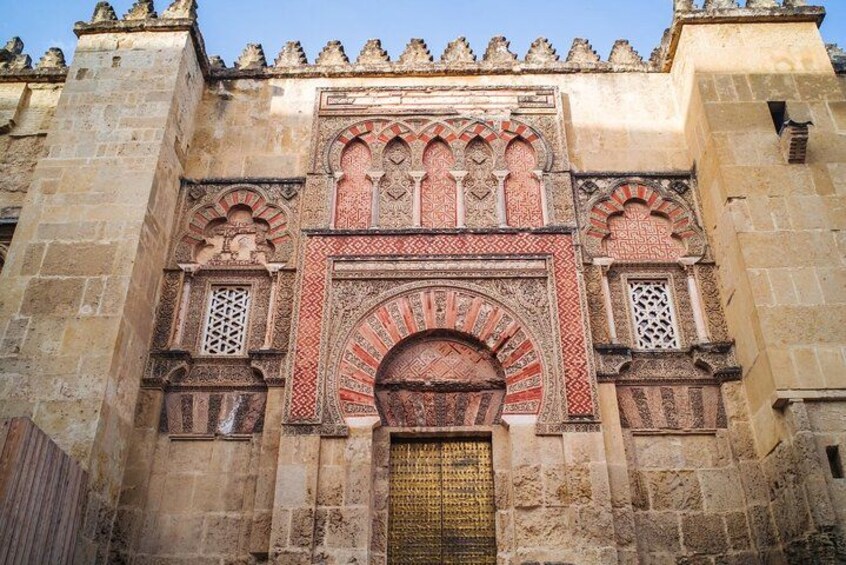 Un bâtiment historique doté d’arcs complexes aux motifs rouges et blancs et d’une grande porte d’entrée centrale. 2