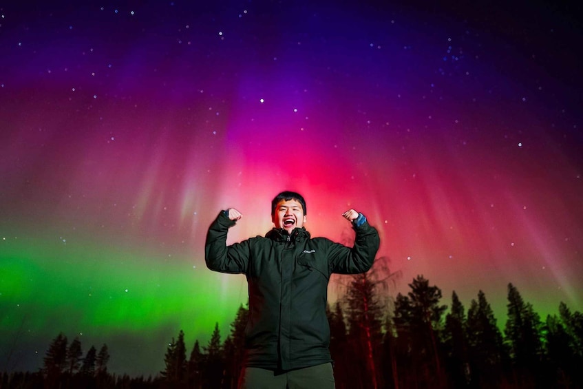 A person with arms raised under a colorful aurora borealis. 1