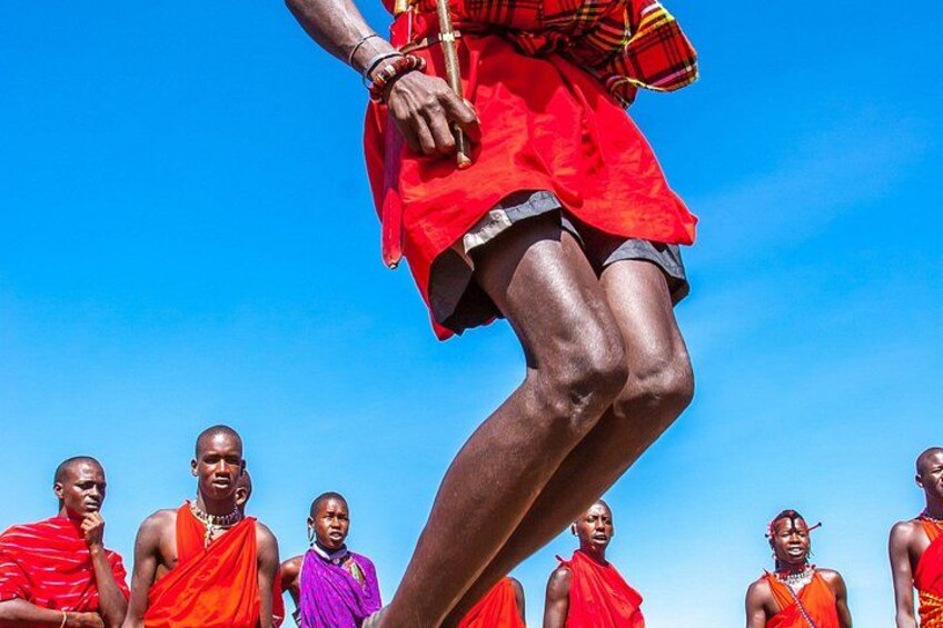 A person in a red outfit with a raised leg, surrounded by individuals in traditional attire. 4