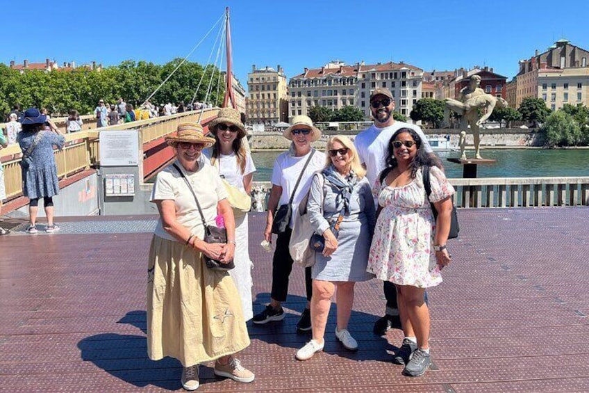 A group of people standing on a bridge with a river and buildings in the background. 1