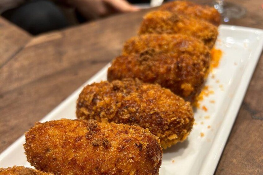 Un plato de porciones de comida empanizada y frita, probablemente croquetas, dispuesto sobre un plato blanco rectangular. 2