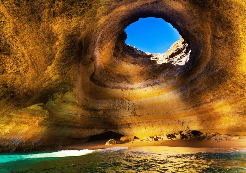 A large cave opening to a beach with clear blue water. 1
