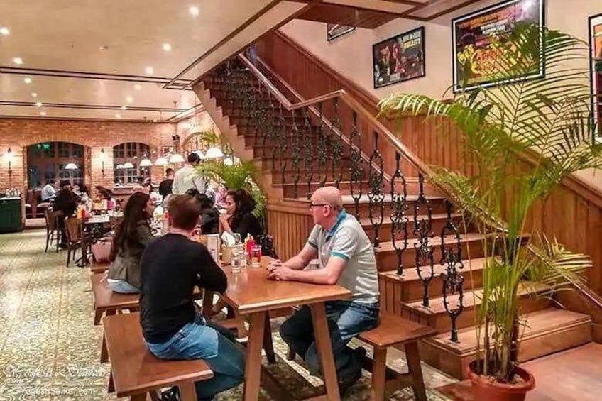A restaurant with wooden tables and chairs, a staircase, and potted plants. 3