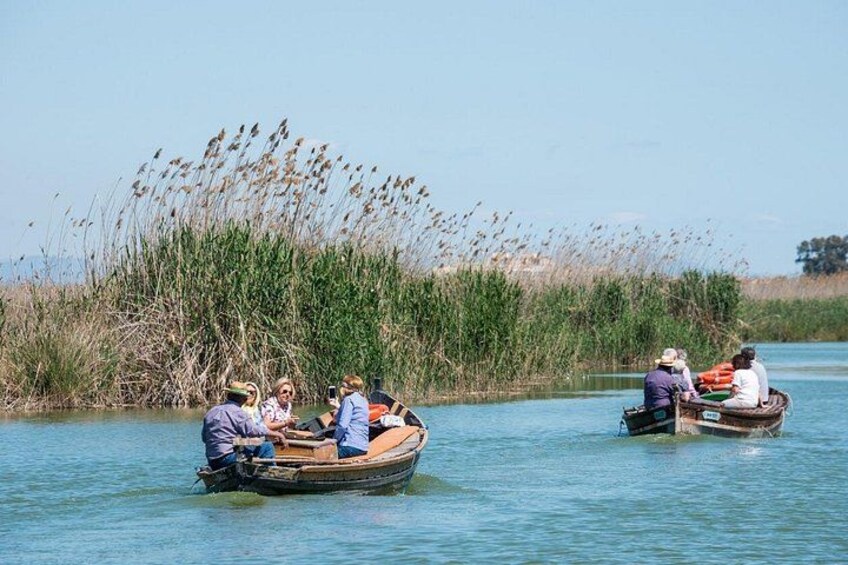 Two small boats on a calm river with people in them, surrounded by tall grasses and reeds. 1