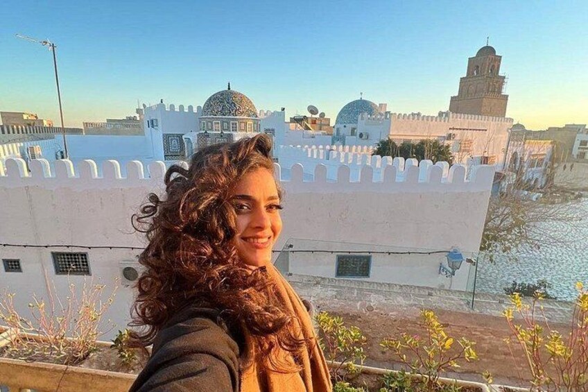 A person with curly hair, a white building with a dome, and a tower in the background. 2