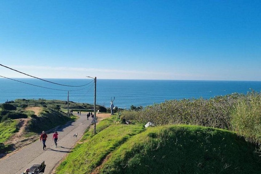A coastal path with people walking, grassy terrain, and a view of the sea. 3