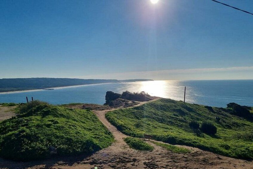 A coastal landscape with a dirt path, grassy hills, and a view of the ocean under a clear sky. 4