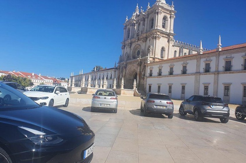 A parking area with several cars, a large historic building with a bell tower, and a clear blue sky. 1