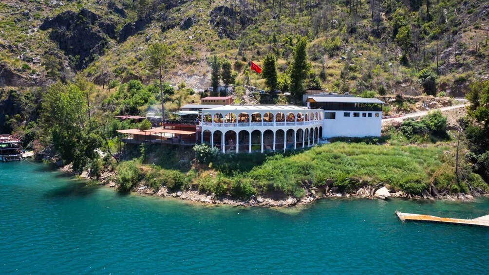 A coastal resort with a white building featuring a white fence, a red flag, and a boat docked nearby. 4