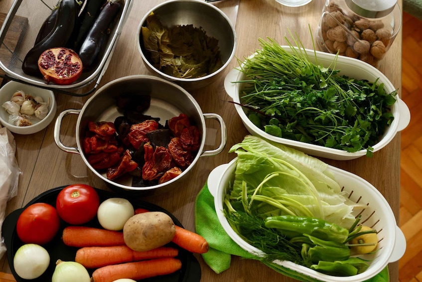 A variety of fresh vegetables and herbs, including tomatoes, carrots, onions, garlic, and leafy greens, arranged on a wooden table. 4