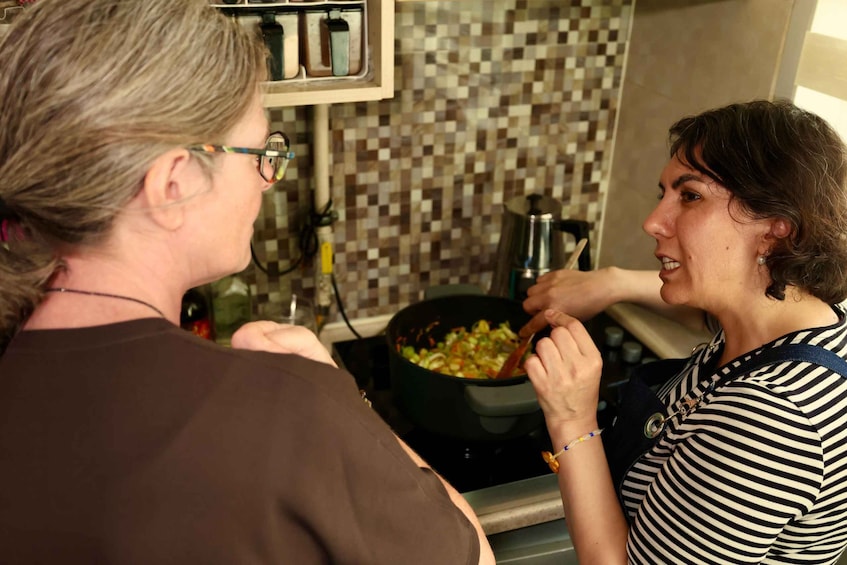 Two people cooking together in a kitchen with a tiled backsplash and a stove. 2
