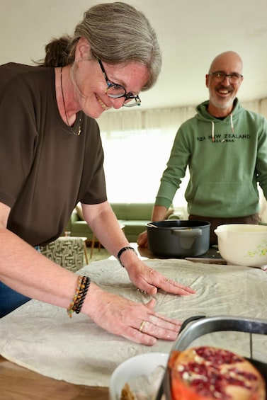 Two people preparing food, one wearing a brown shirt and the other a green hoodie, with a bowl of fruit and a pot on the table. 3