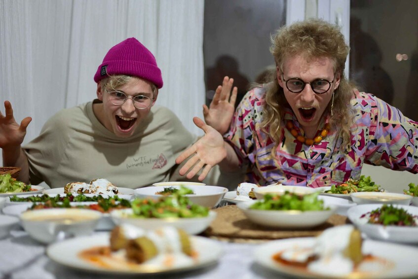 Two people at a dining table with various dishes and a white curtain in the background. 5