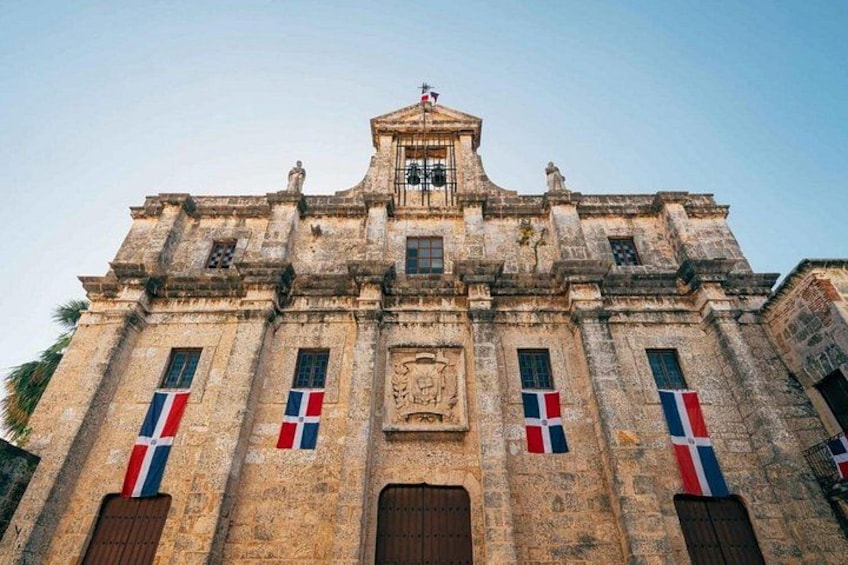 Un edificio histórico con un frontón central, flanqueado por ventanas con banderas francesas y una fachada de piedra detallada. 5