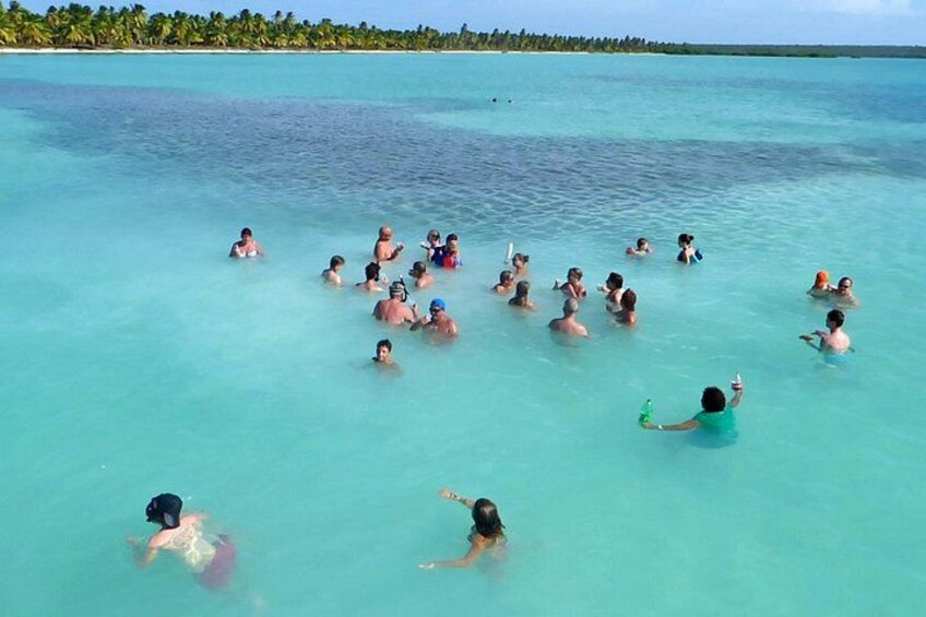 Folk svømmer i klart turkis vand med en strand og palmer i baggrunden. 4