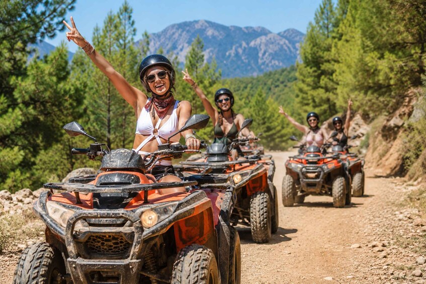 A group of people riding ATVs on a dirt path surrounded by trees and mountains. 1