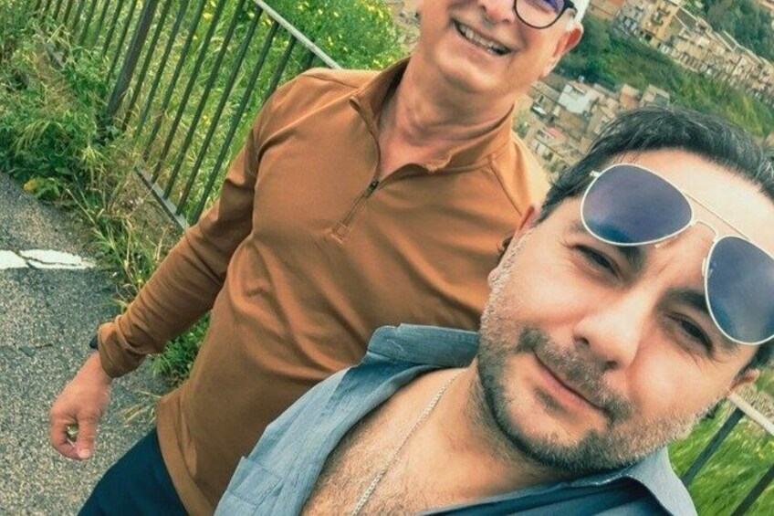 Dos personas de pie en un sendero, con follaje y una valla al fondo. 2
