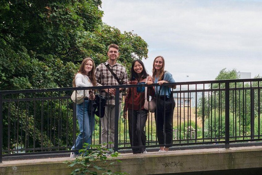 A group of people standing on a bridge with greenery in the background. 1