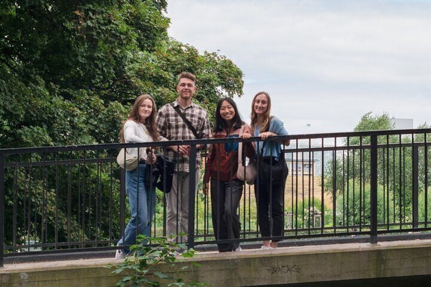 A group of people standing on a bridge with greenery in the background. 1